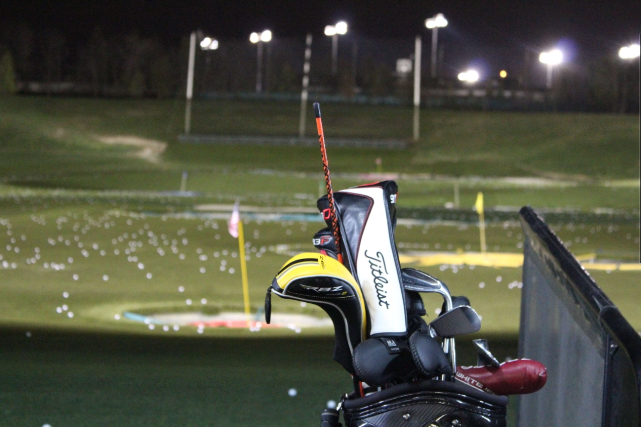 Set of golf clubs set up at the driving range at night time with a blurred background